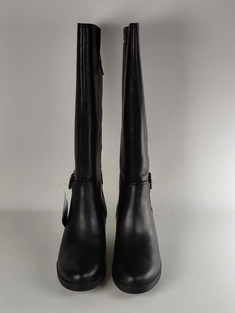 A pair of black leather knee-high boots with side zippers and buckle details, shown against a neutral gray background.