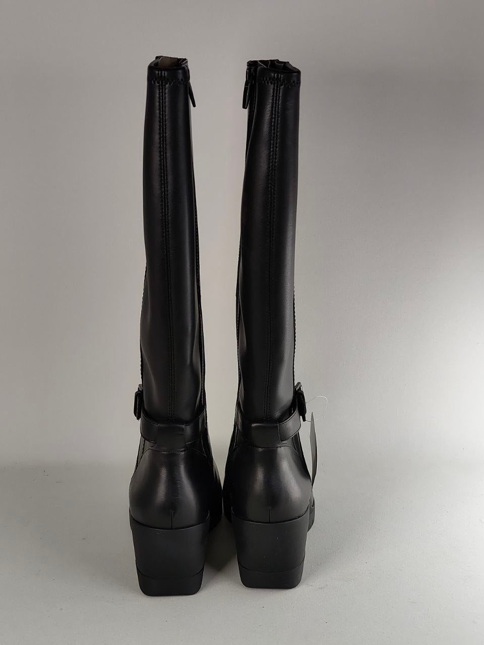 A pair of black leather knee-high boots with side buckle straps, shown from the back against a neutral gray studio background.