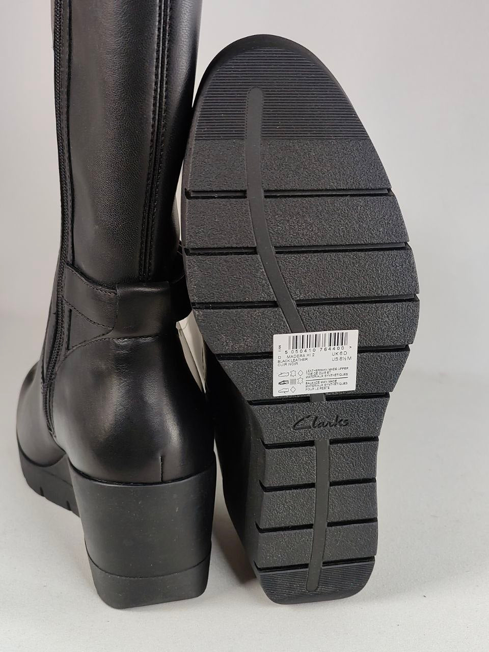 Black leather knee-high boot shown from the back with its sole facing forward, displaying a textured tread pattern and a Clarks brand label on the bottom.