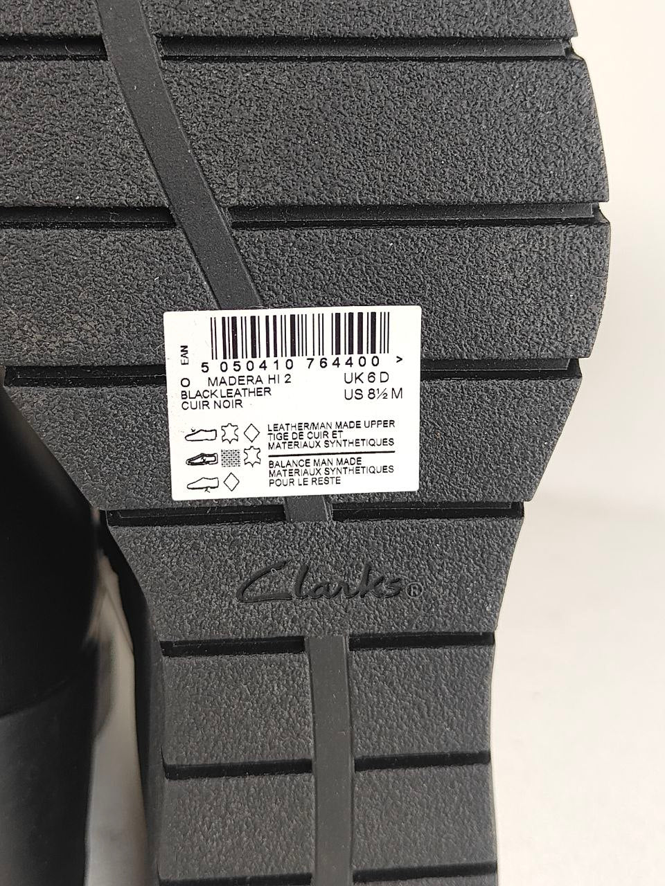 Close-up of the black textured sole of a Clarks shoe, showing a white product label with barcode and size information, and the Clarks logo embossed near the bottom.