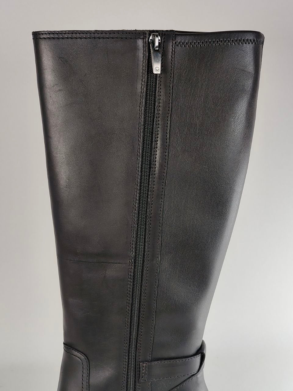 A close-up of a black leather knee-high boot featuring a central metal zipper running from the top opening to the ankle.