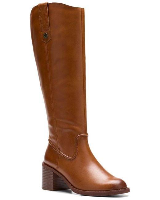 A tall brown leather knee-high boot with a block heel and a small decorative metal rivet near the top, shown against a plain white background.