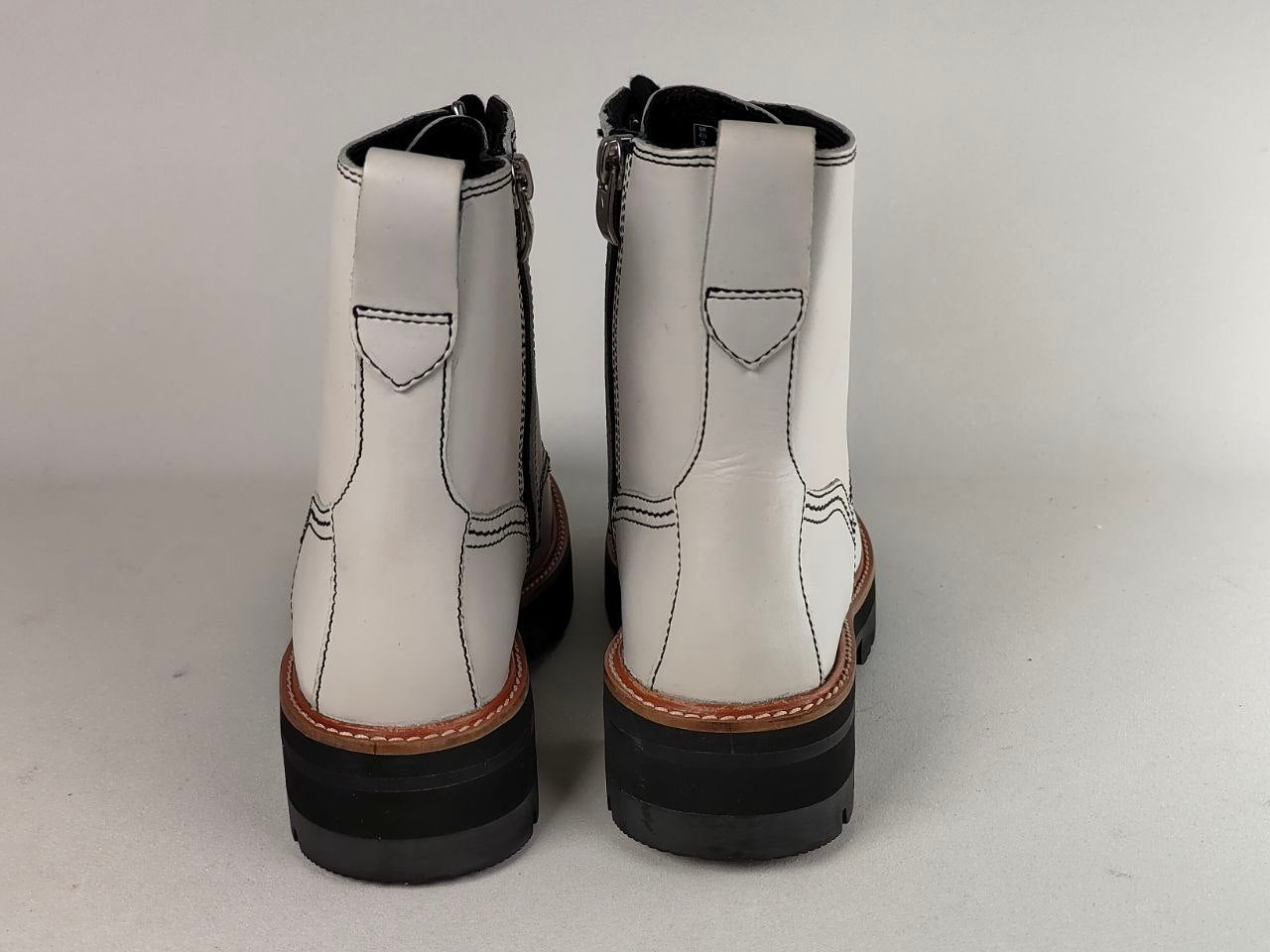 A pair of white leather ankle boots with black soles and side zippers, shown from the back against a neutral light gray background.