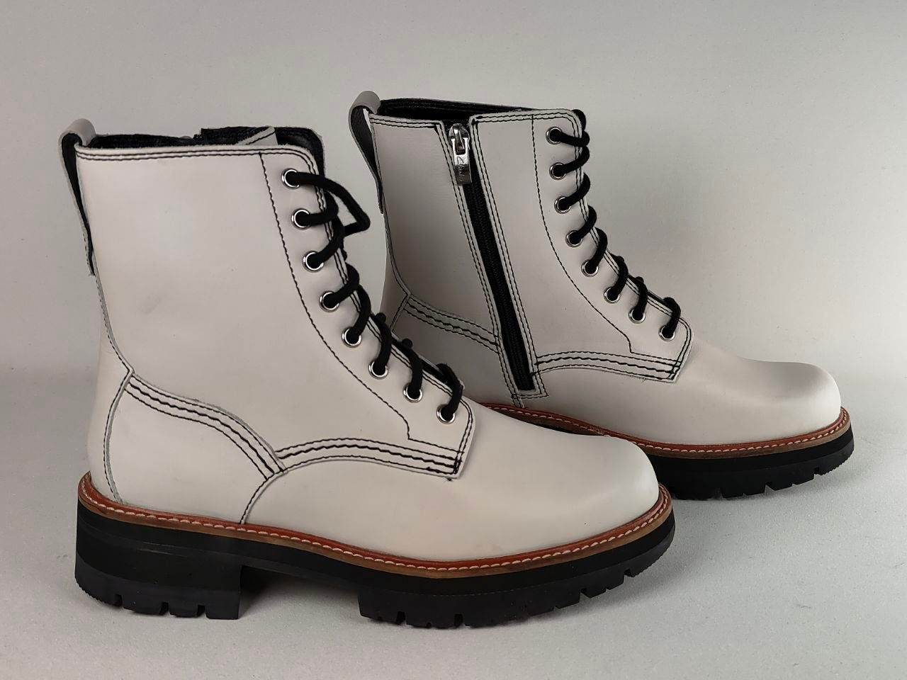 A pair of white leather lace-up ankle boots with black laces, black soles, and a side zipper, shown on a light gray background.