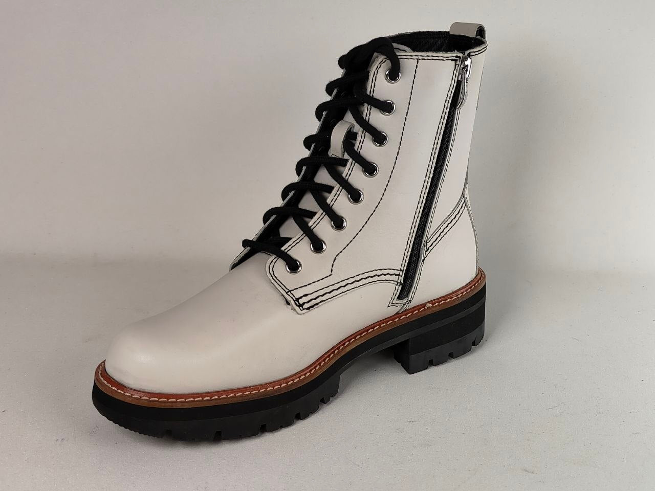 A white leather lace-up ankle boot with black laces, a black sole, and a visible side zipper, photographed on a light gray studio background.