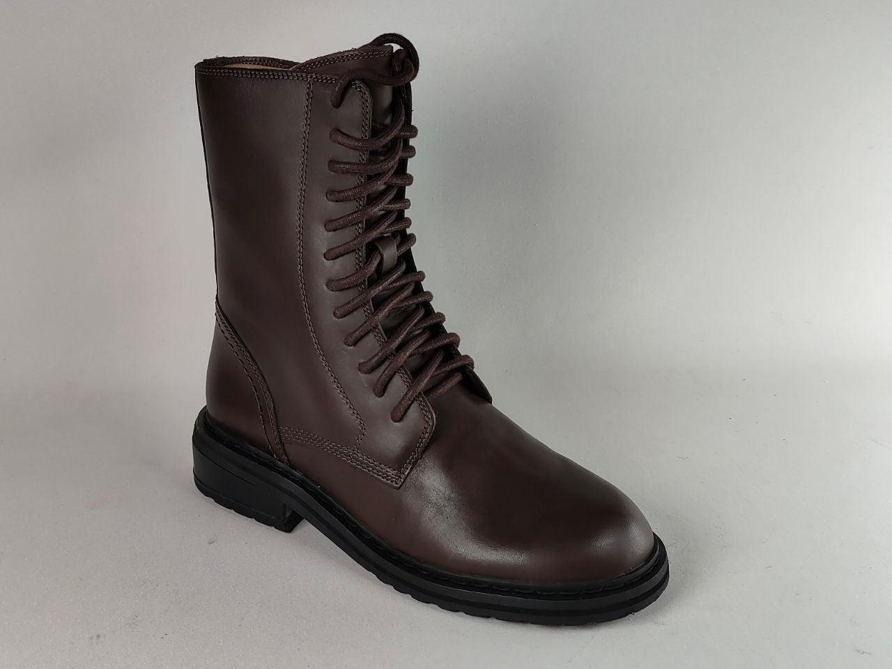 A dark brown leather lace-up boot with a black sole, photographed on a neutral light gray background.