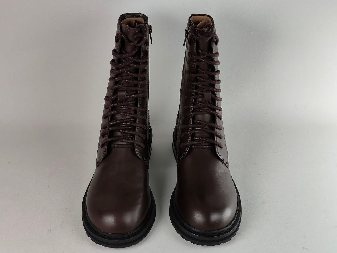 A pair of dark brown leather lace-up boots with black soles, photographed against a neutral light gray background.