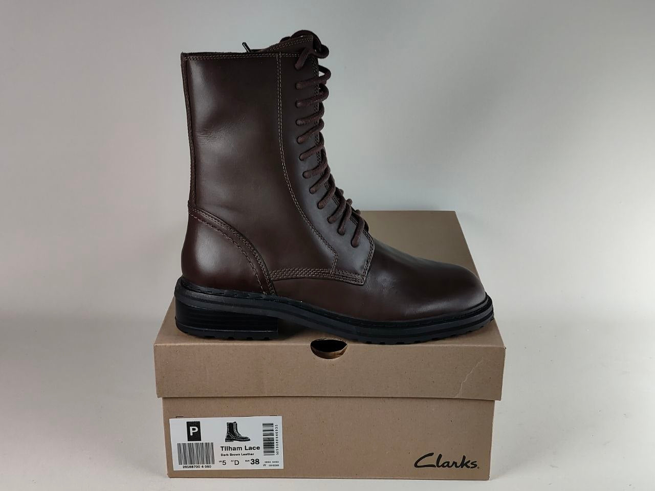 A dark brown leather lace-up boot by Clarks, displayed on top of its brown cardboard shoebox against a neutral light gray background.