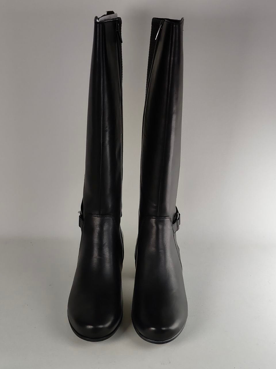A pair of black leather knee-high boots with side buckle details, photographed against a neutral gray background.