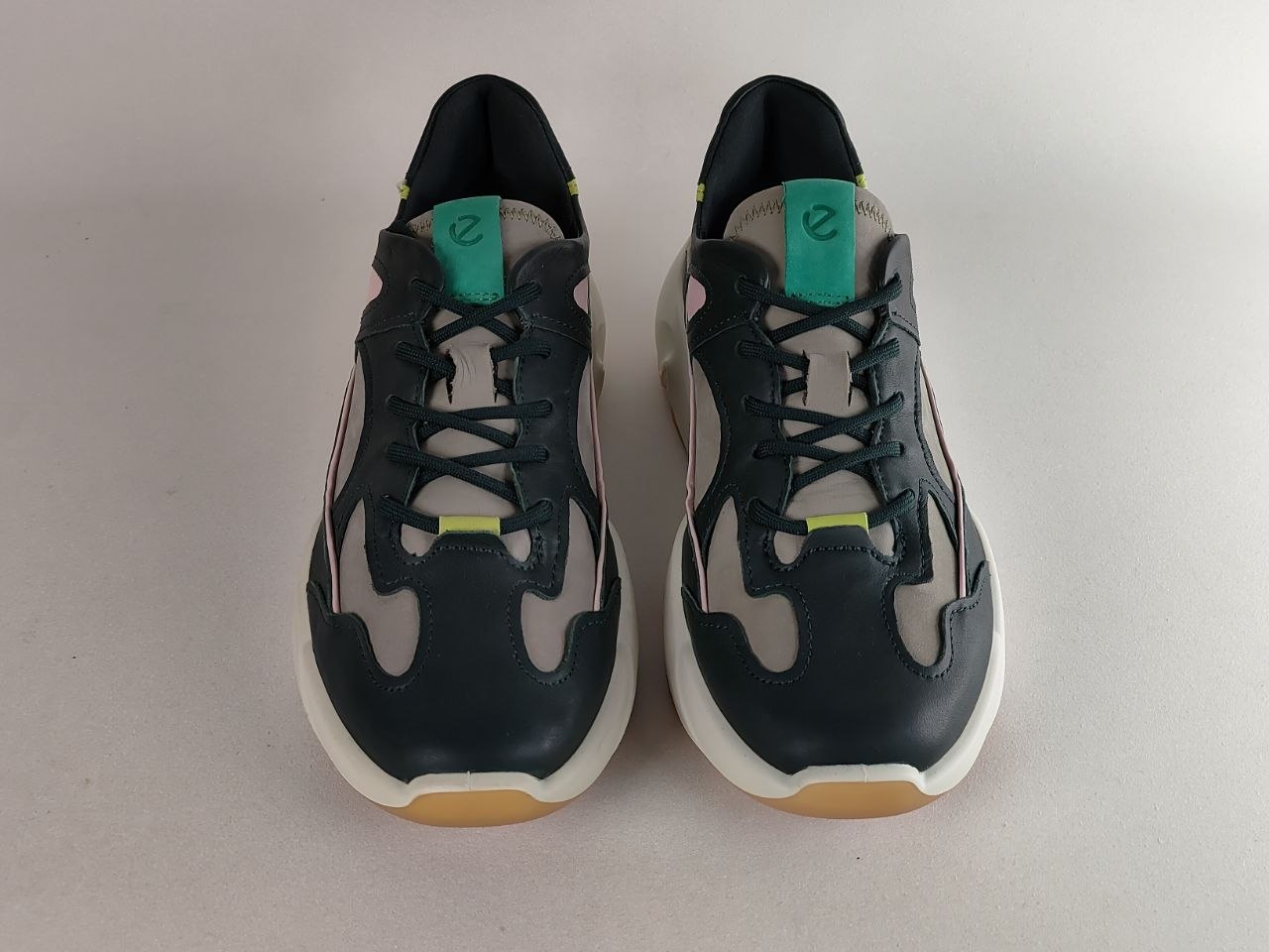 A pair of low-top sneakers shown from the front on a light gray background. The shoes feature a dark navy blue leather upper with light gray mesh panels, white midsoles, and small lime green accents on the tongue and around the eyelets.