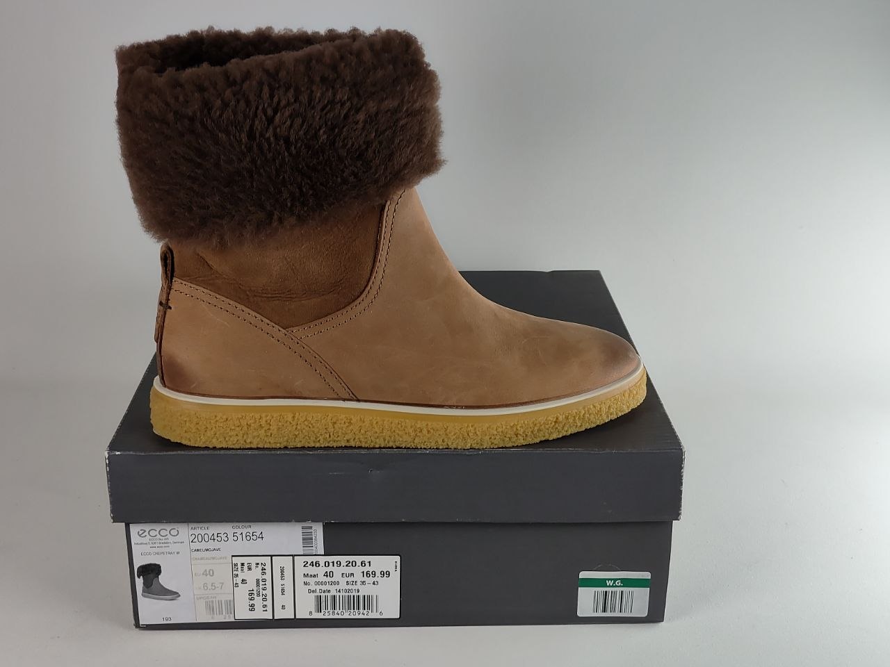 A tan suede ankle boot with a dark brown faux-fur trim, resting on top of its black ECCO shoebox against a light gray background.