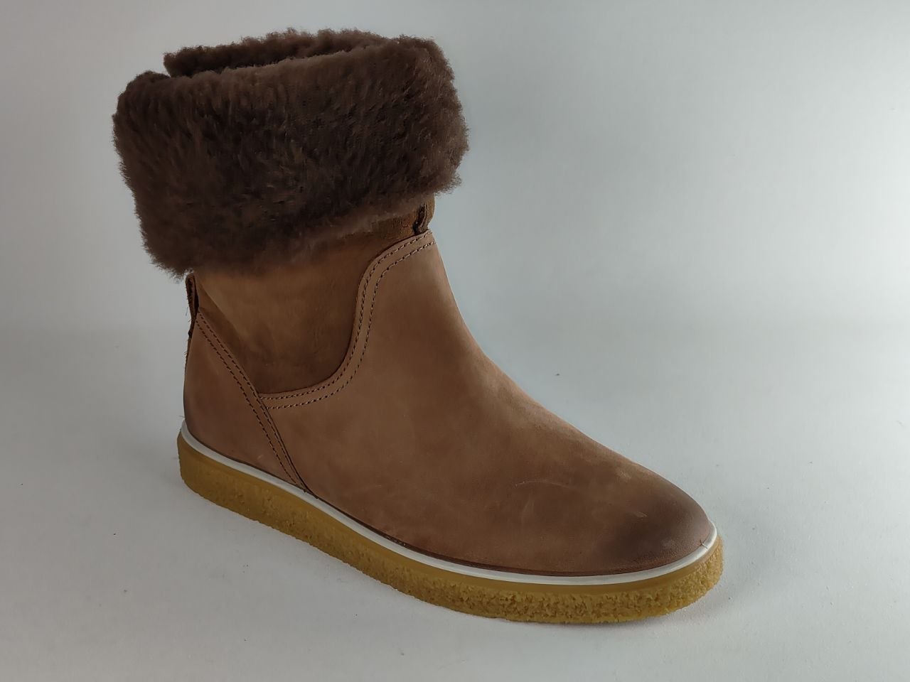 A brown suede ankle boot with a thick brown faux-fur collar and a tan rubber sole, shown from a side profile on a light gray background.