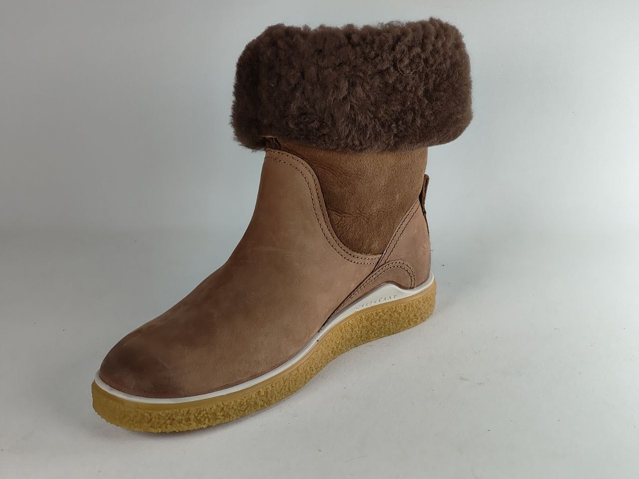 A brown suede slip-on boot with a thick brown shearling-style collar and a tan rubber sole, photographed on a light gray studio background.