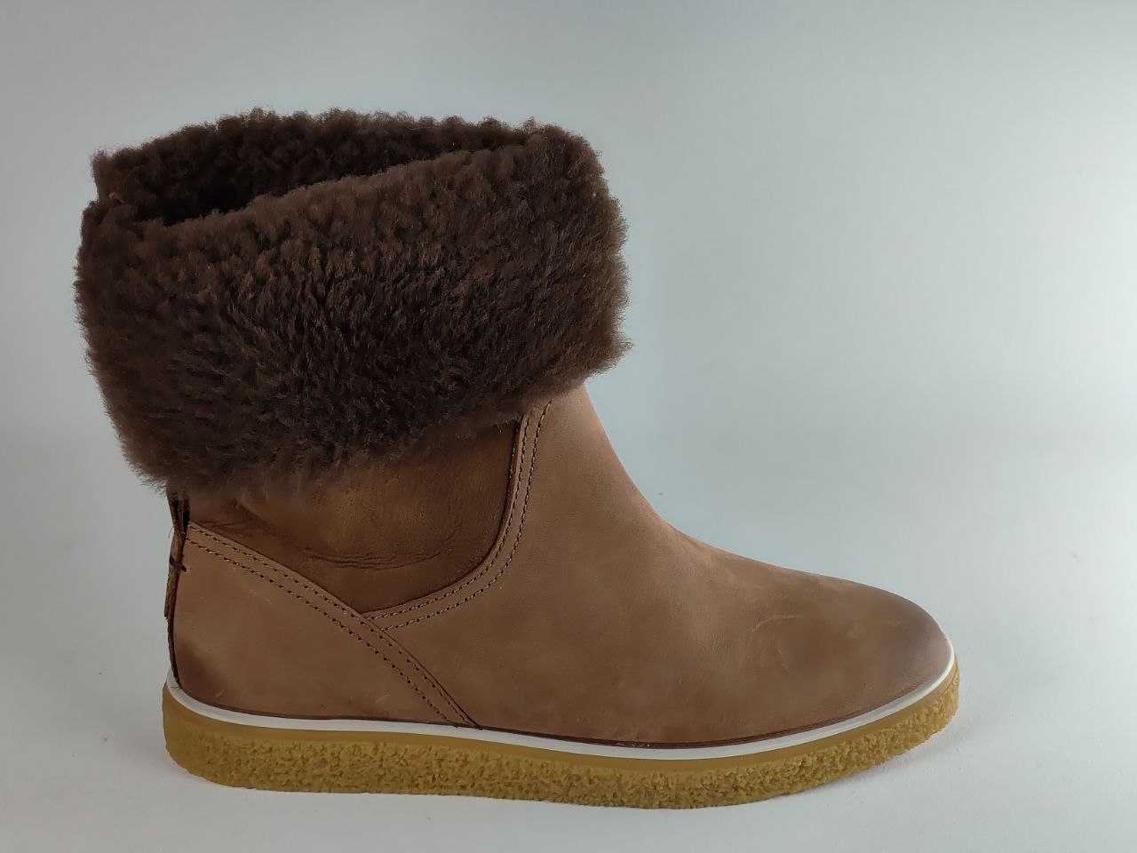 A brown suede ankle boot with a thick, fluffy dark brown faux-shearling cuff and a tan rubber sole, shown from a side profile on a light gray background.