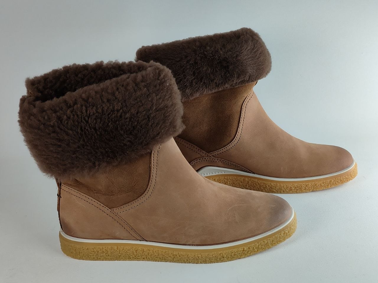 A pair of brown suede ankle boots with thick, fluffy dark brown faux-fur cuffs and tan rubber soles, shown on a light gray background.