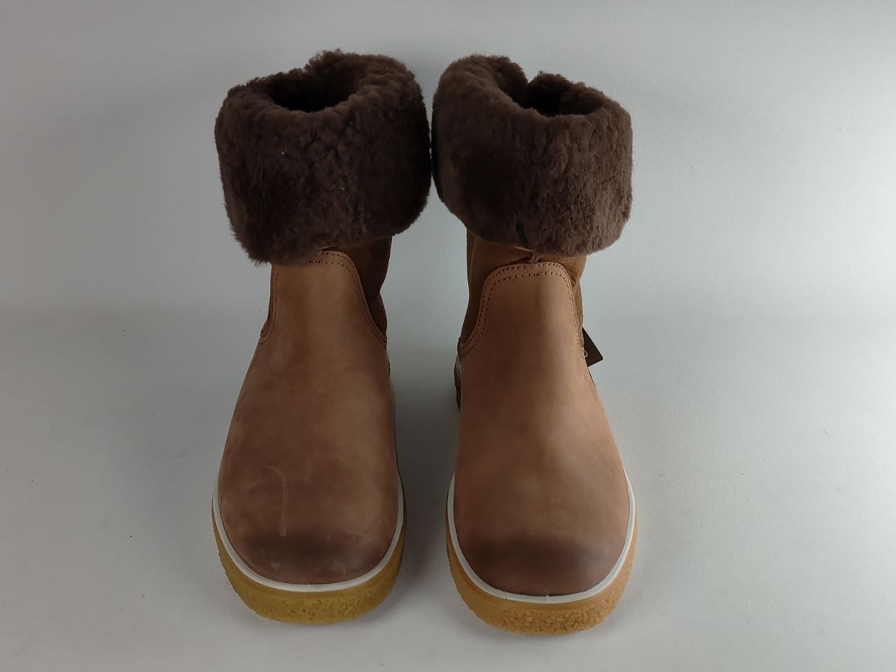 A pair of women's ankle boots in tan leather with a thick brown faux-fur collar and a yellow-brown sole, shown from a front-facing perspective on a light gray background.