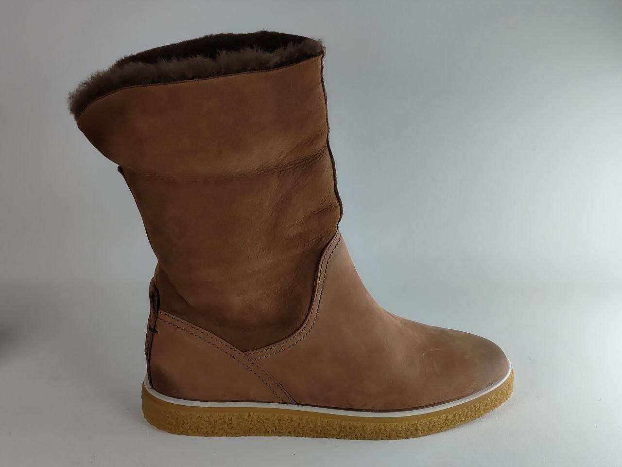A mid-calf brown suede boot with a dark brown faux-fur lining at the collar and a tan rubber sole, shown from a side profile against a light gray background.