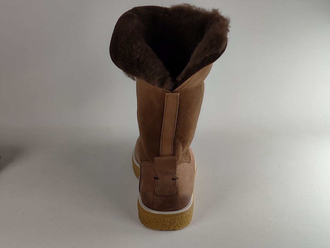 A single mid-calf boot shown from the back, featuring a tan suede upper, a dark brown shearling-style lining, and a tan rubber sole.