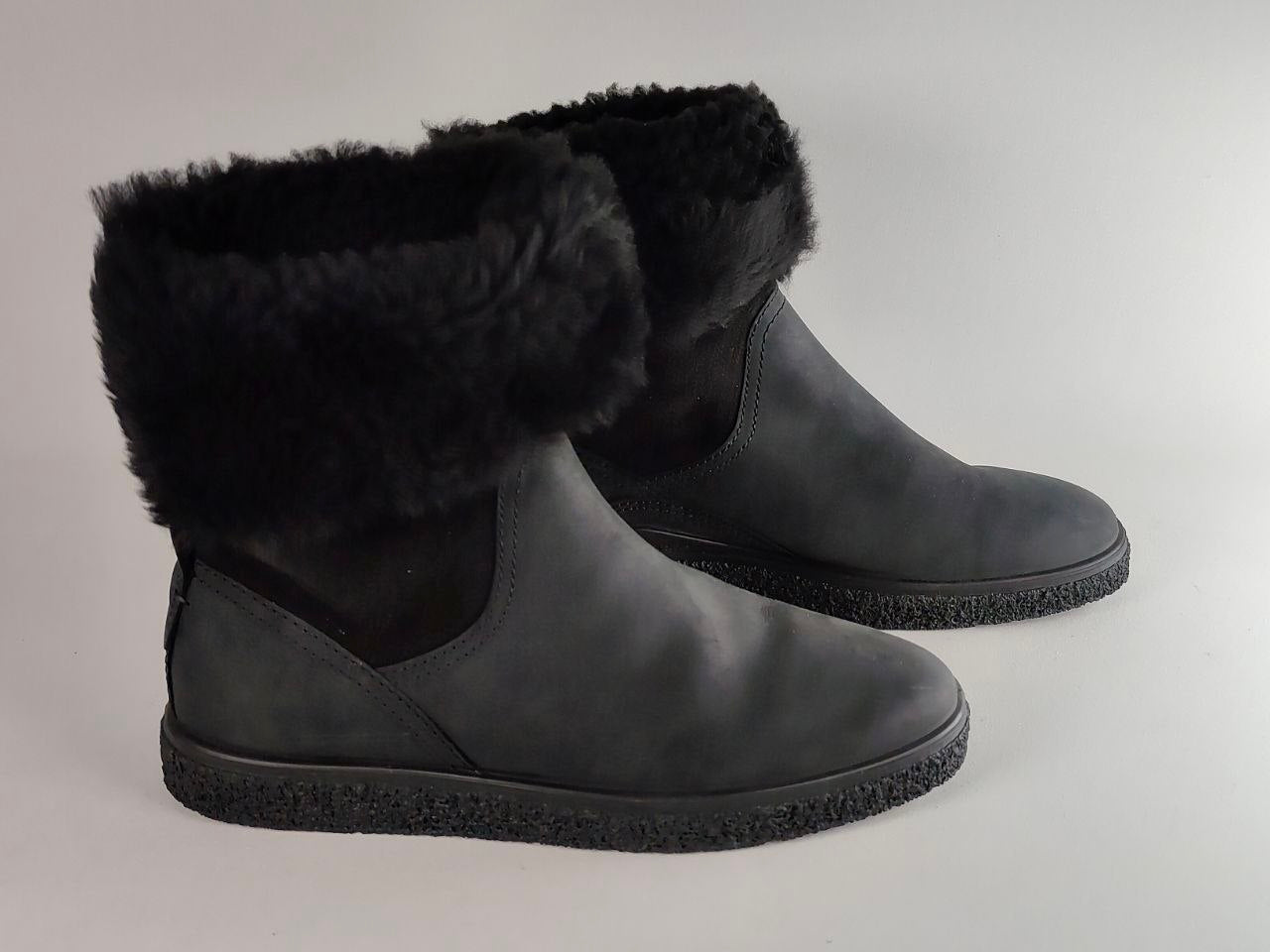A pair of black ankle boots with plush black faux-fur trim around the collar, shown on a neutral light gray background.
