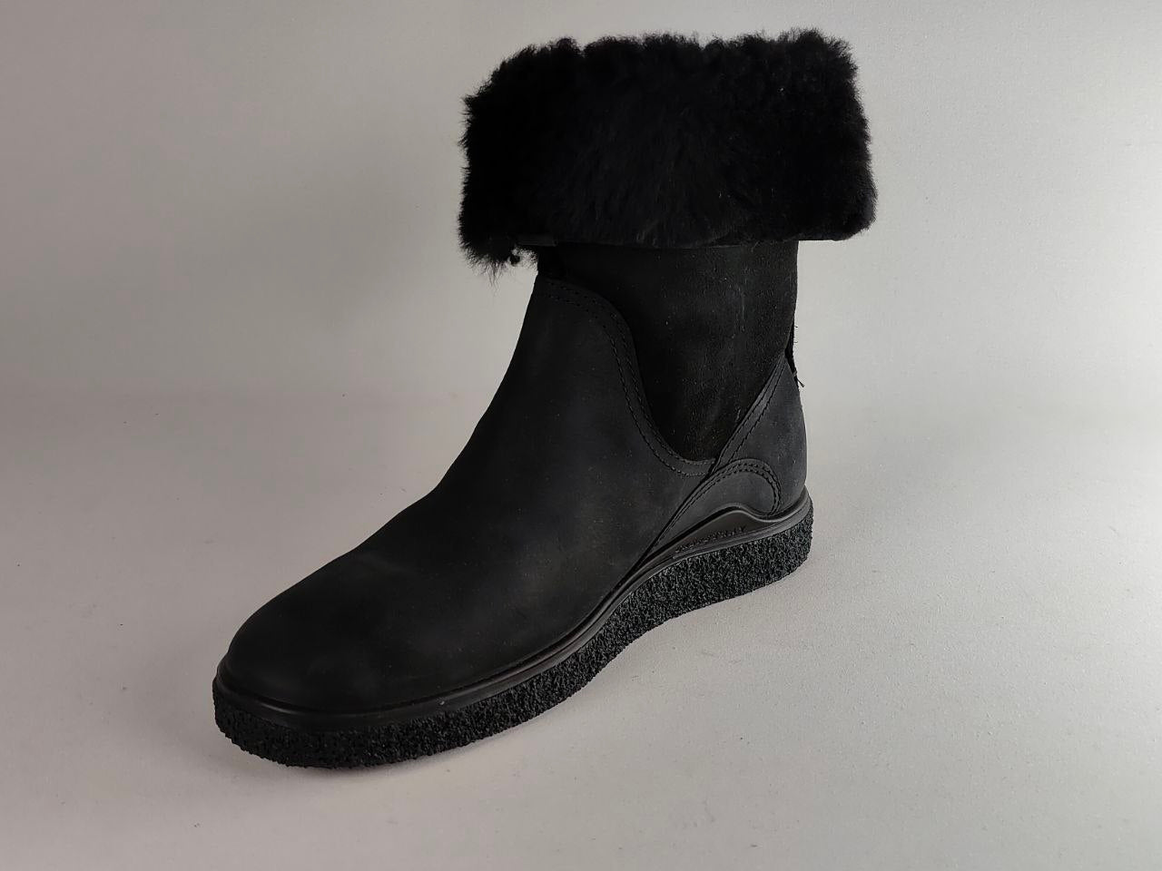 A black ankle boot with a soft black faux-shearling cuff, photographed on a neutral light gray background.