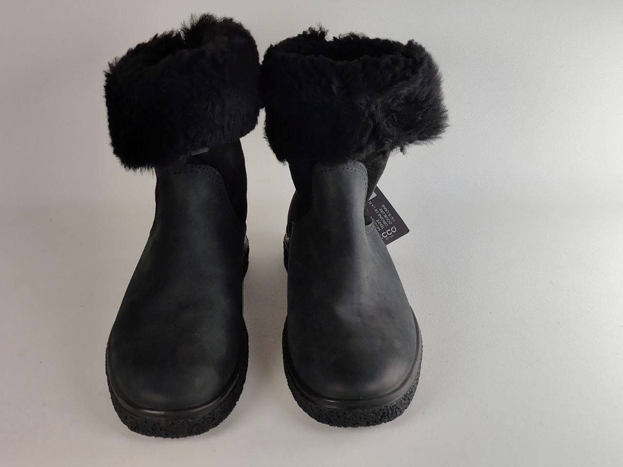 A pair of black ankle boots with fluffy black faux-fur trim around the cuffs, shown against a light gray background.