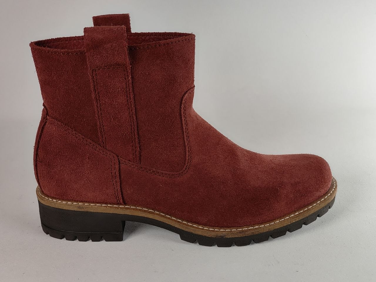 A single red suede Chelsea-style ankle boot with a pull tab, set against a plain light gray background.