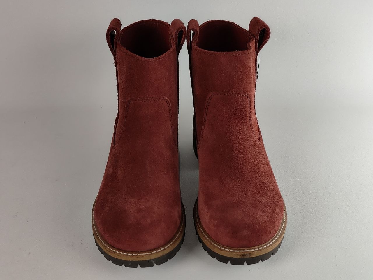 A pair of women's ankle boots in dark red suede, featuring elastic side panels and pull tabs, with tan and black soles, shown against a neutral gray background.