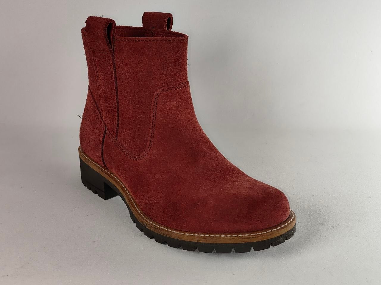 A single women's ankle boot in dark red suede, featuring a pull tab, elastic side gore, and a chunky black lug sole with a tan welt.