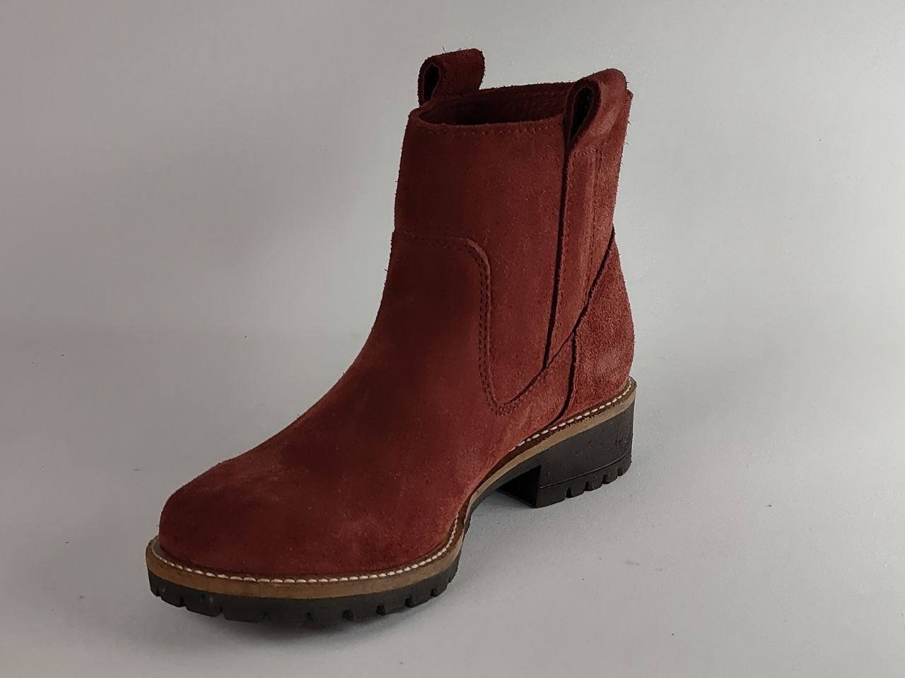 A single women's ankle boot in dark red suede, featuring a low block heel, elastic side gore, and a rugged black lug sole, shown against a neutral gray background.