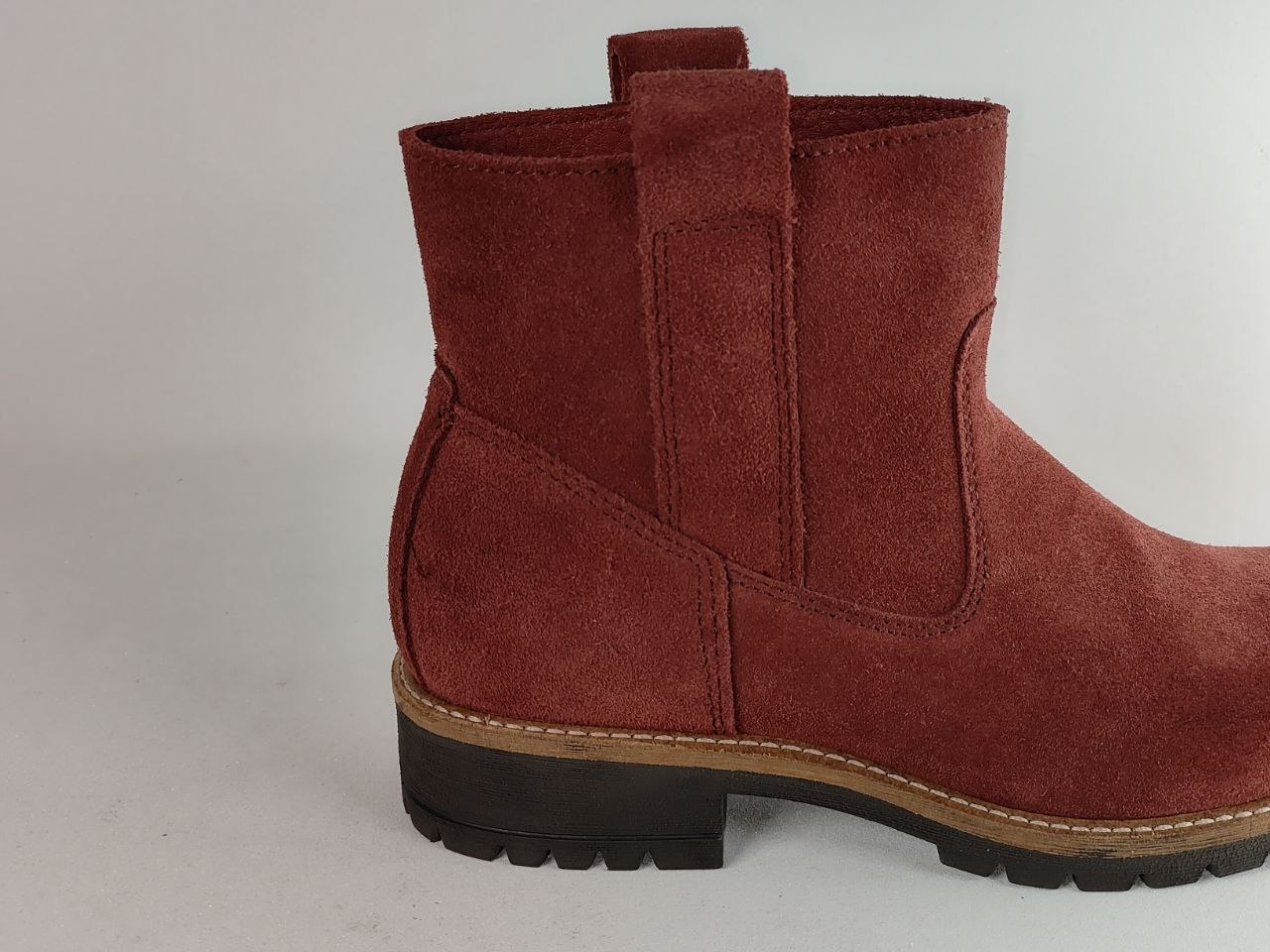 A single dark red suede Chelsea-style ankle boot with a black lug sole and tan midsole, shown from a side profile against a light gray background.