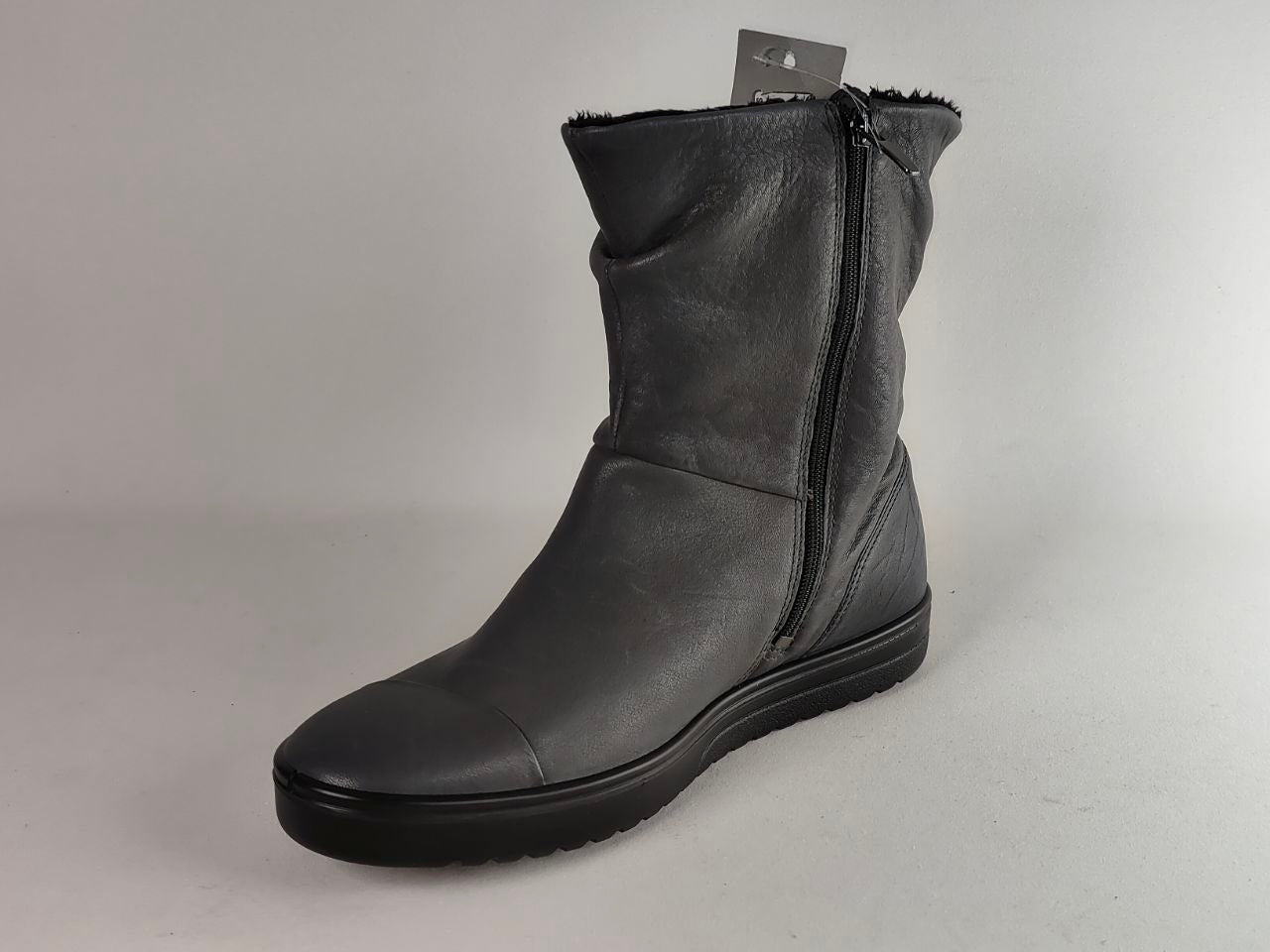 A single black leather ankle boot with a side zipper, shown on a neutral light gray background. A small hangtag is attached near the collar.
