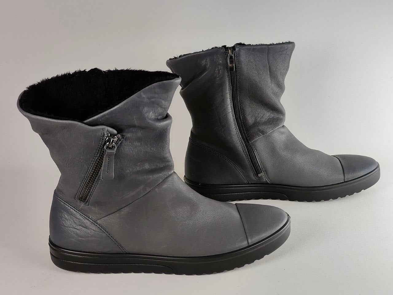 A pair of dark gray leather ankle boots with black soles and black faux-fur lining, shown on a neutral light gray background.