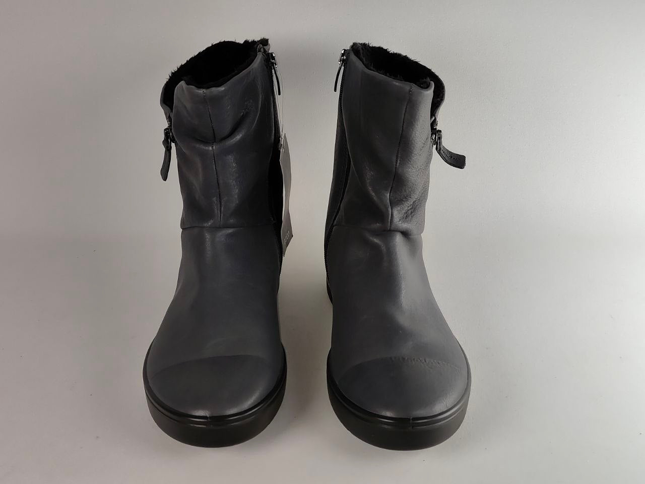 A pair of black leather ankle boots with side zippers and a fuzzy black lining, shown from the front on a light gray background.