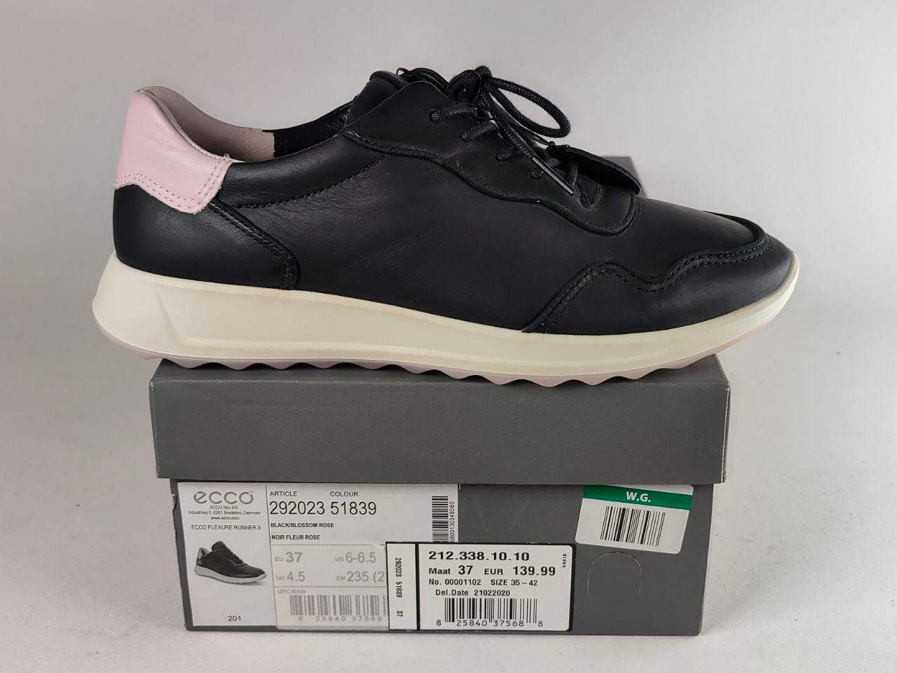 A black leather low-top sneaker with a light pink heel tab and a thick cream-colored midsole, displayed on top of its gray ECCO shoebox against a light gray background.