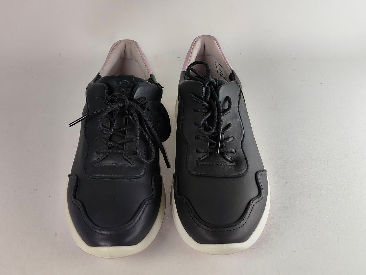 A pair of black leather low-top sneakers with black laces and thick white soles, photographed against a neutral light gray background.