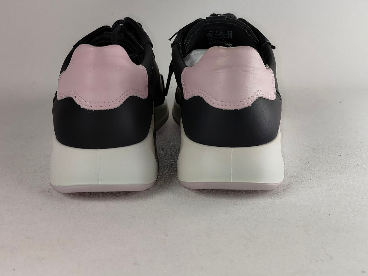 A pair of black and light pink sneakers shown from the back, featuring a black leather upper, a light pink leather heel tab, and a thick white midsole.