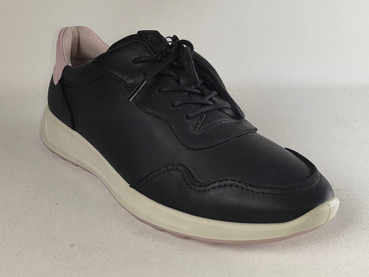 A black leather low-top sneaker with black laces, a thick off-white sole, and a light pink inner lining visible at the heel, shown on a neutral light gray background.