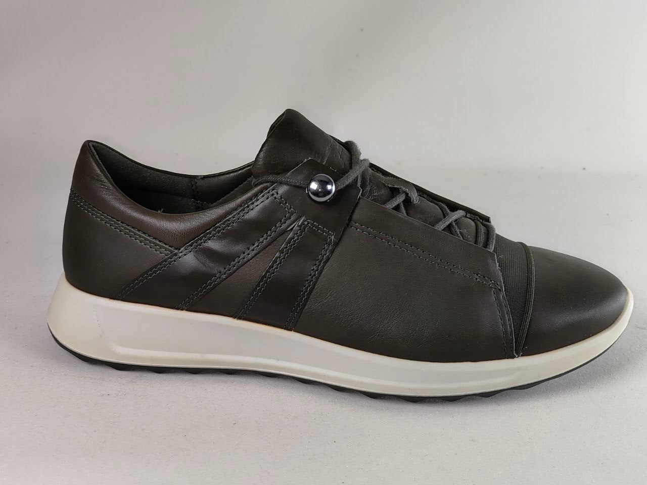 A dark brown leather low-top sneaker with a white sole, featuring a decorative silver metal rivet on the side and matching dark brown laces, shown against a neutral light gray background.