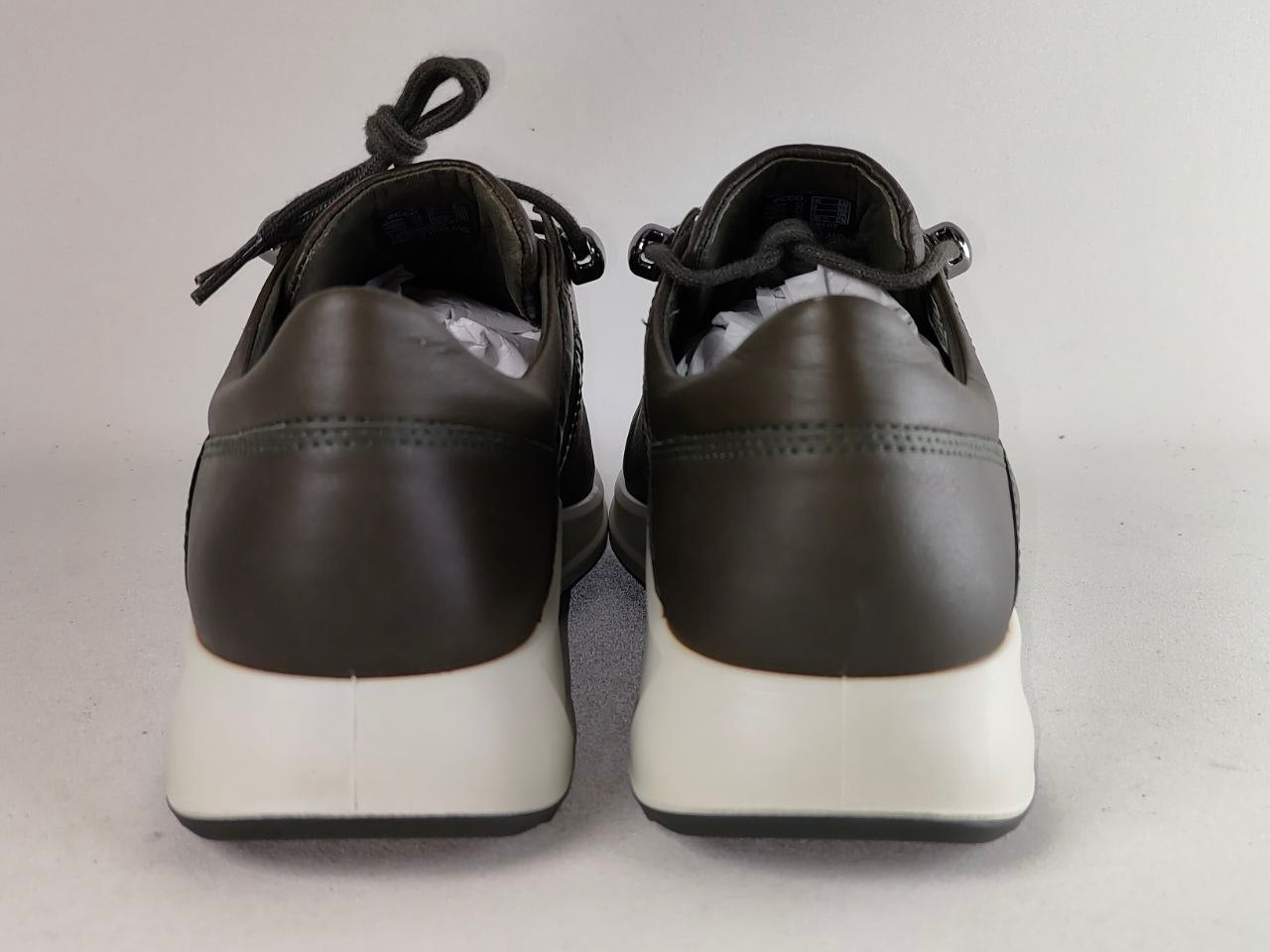 A pair of dark brown leather lace-up sneakers shown from the back, featuring thick white platform soles and black laces, set against a plain light gray background.
