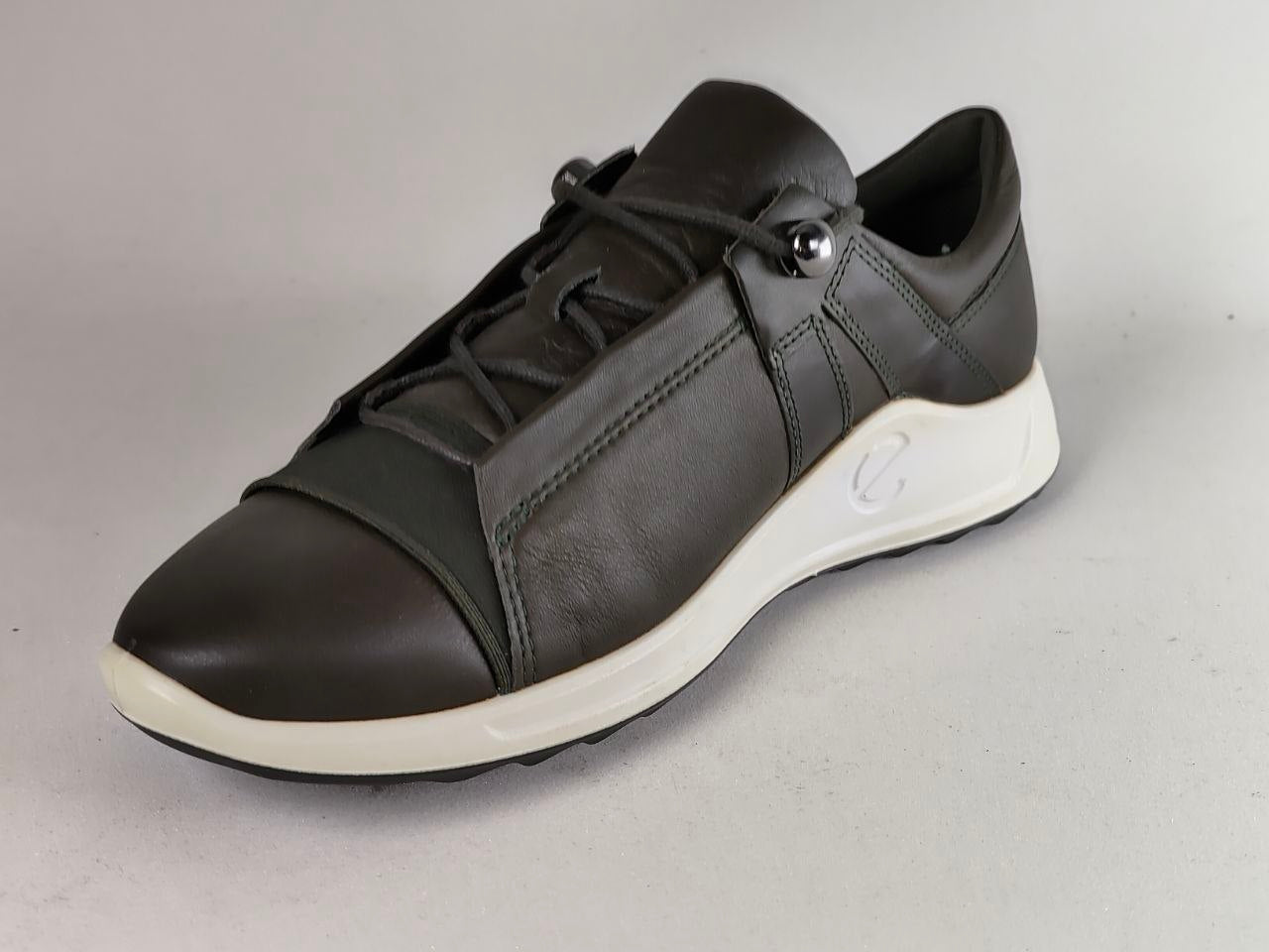 A black leather athletic sneaker with a white midsole and a small silver metal accent on the side, photographed against a neutral gray background.
