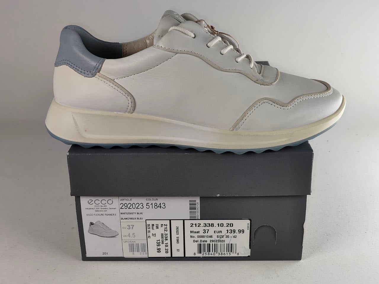 A light gray and white Ecco sneaker with a gray heel tab, resting on top of its dark gray shoebox. The shoebox features the Ecco brand logo and product details.