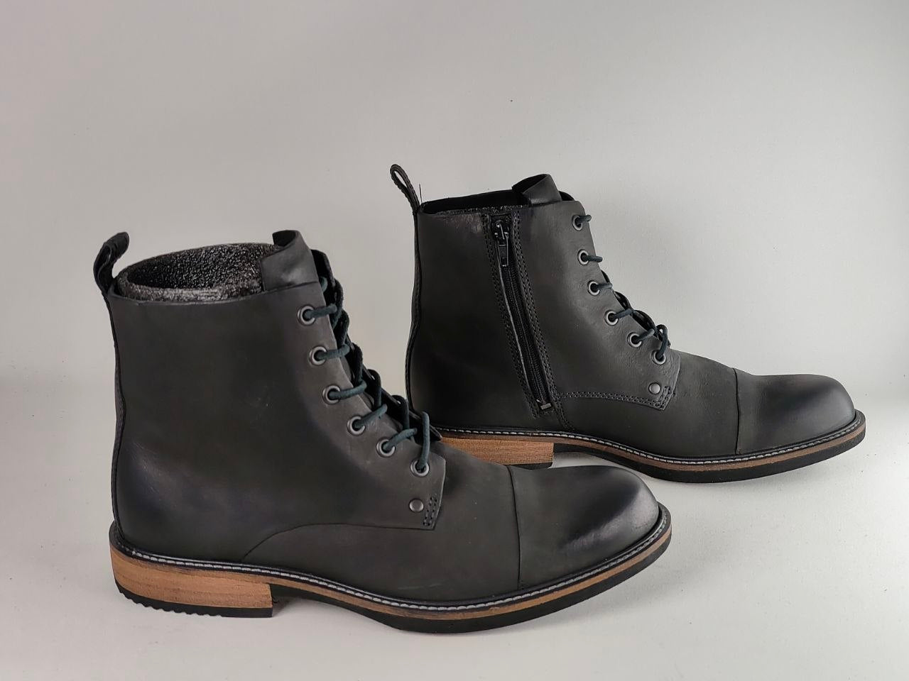 A pair of black leather lace-up ankle boots with a side zipper, shown on a neutral light gray background.