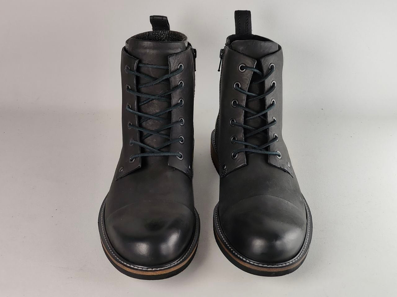 A pair of black leather lace-up ankle boots with side zippers, shown from the front on a light gray background.