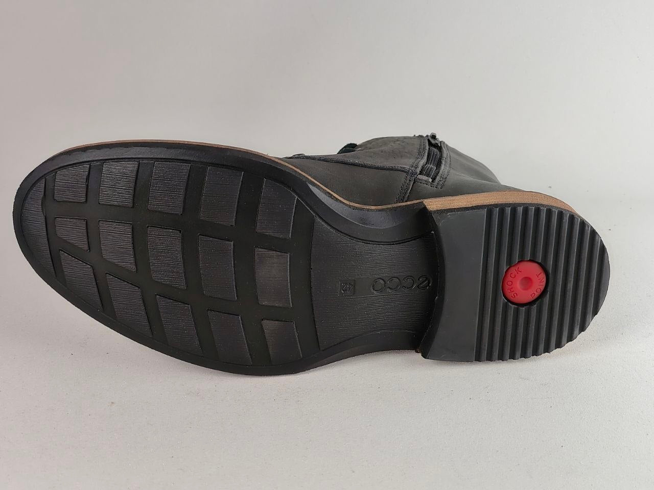 The outsole of a black leather boot, showing the tread pattern, embossed brand name, and a small red circular detail on the heel.