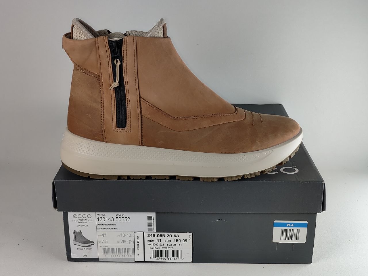 A tan suede ankle boot with a black side zipper, resting on top of its dark gray ECCO shoebox against a light gray background.