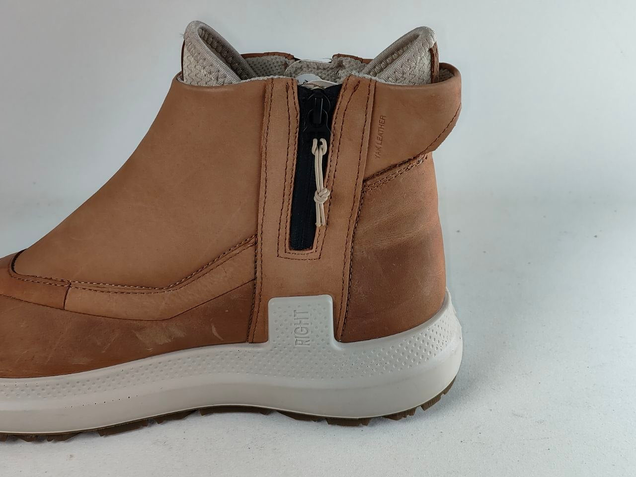 A tan suede ankle boot with a side zipper, a thick white sole, and a light gray textured lining, shown from a side profile view against a light gray background.