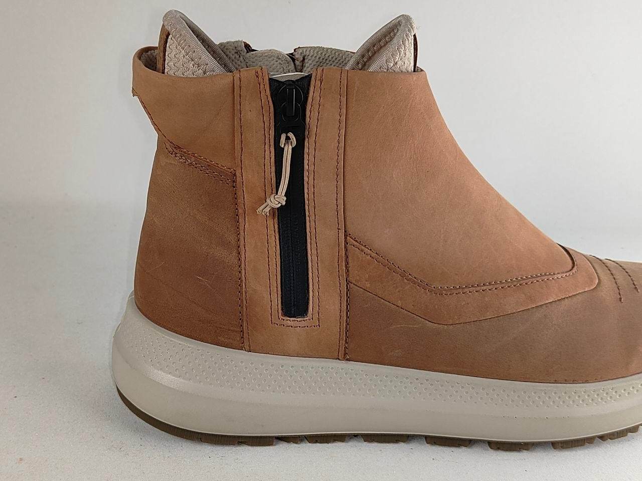 A tan suede ankle boot with a side zipper, a thick off-white sole, and a light beige lining, shown from a side profile view against a plain light background.