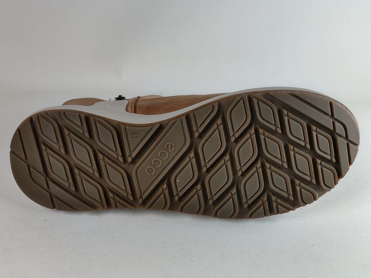 A close-up of the textured brown rubber outsole of a boot, showing the embossed ECCO brand name and a diamond tread pattern, set against a plain light gray background.