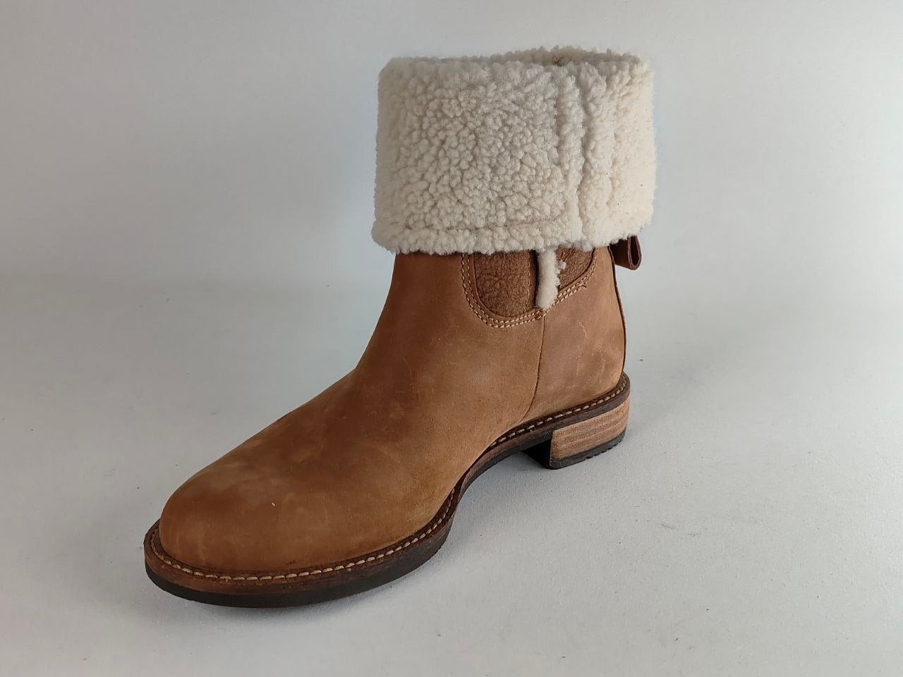 A brown suede ankle boot with a thick, fluffy off-white shearling-style cuff, shown from a side profile on a neutral light gray background.