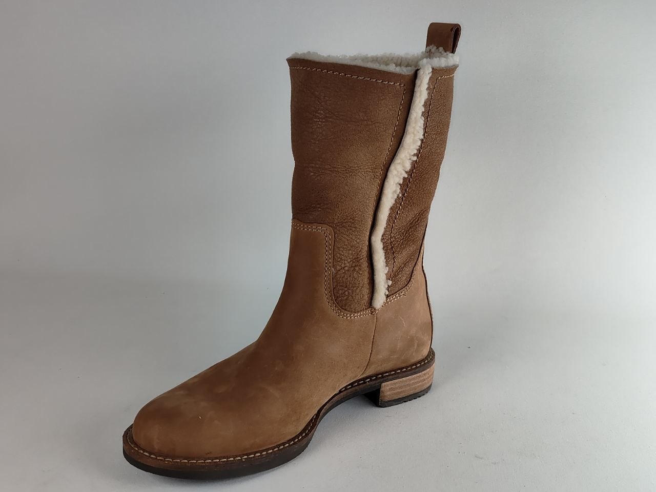 A mid-calf brown suede boot with a white shearling-style lining visible at the opening and side, photographed on a plain light gray studio background.